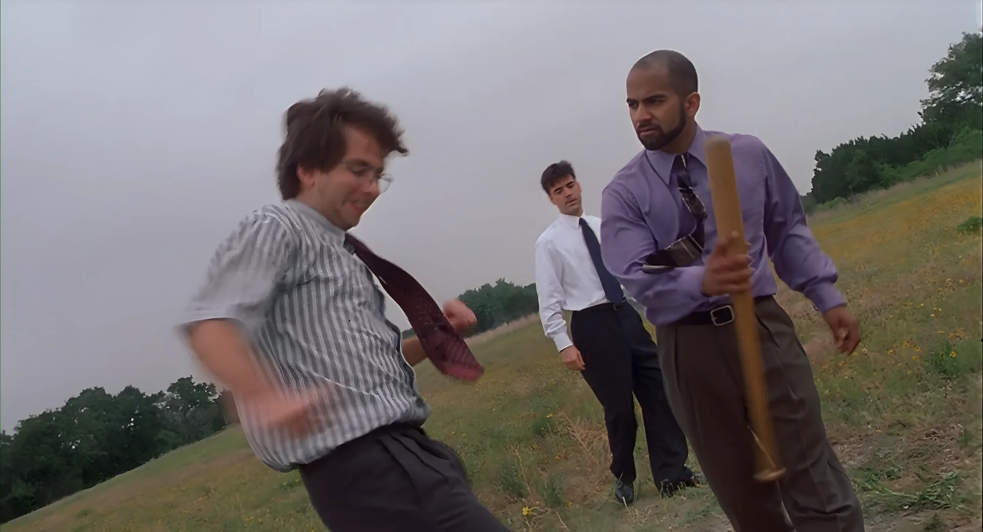 The crew in a field with a baseball bat, about to destroy the printer.