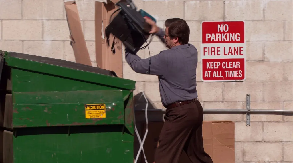 Ron Swanson throwing a computer into a dumpster.